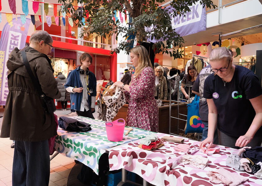 Bezoekers bekijken en ruilen kleding bij een kledingruiltafel tijdens de Klimaatweek in Cpunt, met kleurrijke vlaggetjes en Cpunt-medewerkers